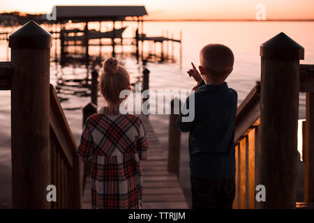 Vue arrière du frère pointant vers le lac alors que l'article de sœur pendant le coucher du soleil Banque D'Images