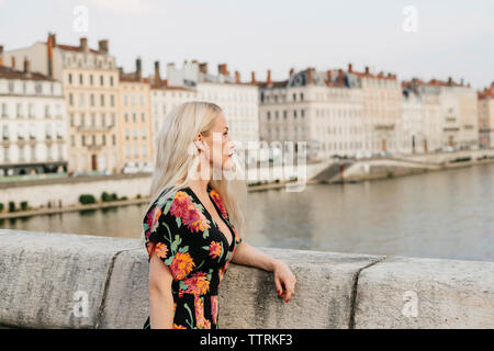 Vue latérale d'une femme debout sur la passerelle sur la rivière contre les bâtiments en ville Banque D'Images