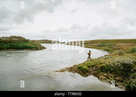 Vue de côté de l'homme dans le lac de pêche contre l'Islande à cloudscape Banque D'Images