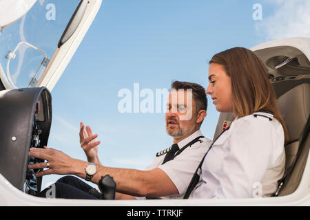 Low angle view of male femelle d'enseignement pilote stagiaire à actionner le panneau en avion à l'aéroport contre le ciel bleu Banque D'Images