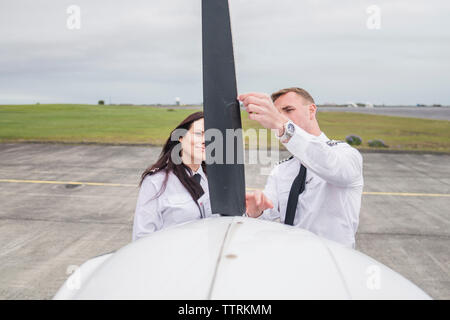 Ingénieur mâle montrant pièces d'avion à femme stagiaire en position debout contre ciel nuageux sur la piste de l'aéroport Banque D'Images
