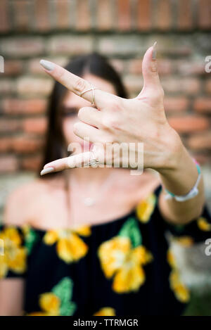 Close-up of woman showing sonne pendant que se tenir contre un mur de briques Banque D'Images