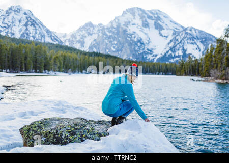 Toute la longueur de femme accroupie sur un rocher au milieu d'un lac gelé contre montagne Banque D'Images