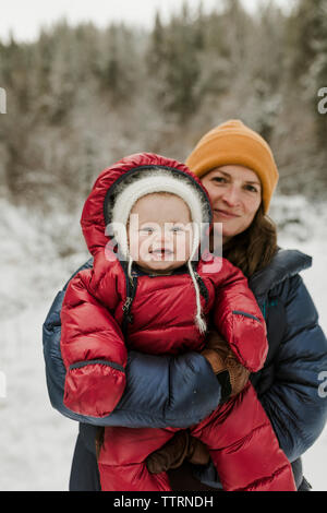 Portrait de mère portant fille debout dans la forêt en hiver Banque D'Images