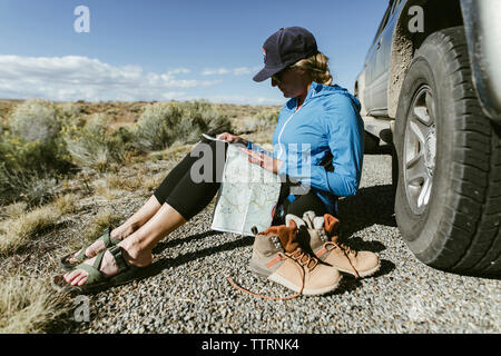 Toute la longueur de female hiker reading map tout en restant assis sur la route en voiture Banque D'Images