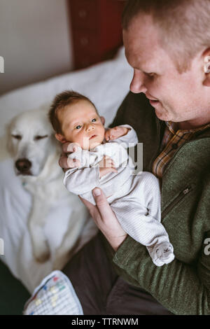 nouveau-père tenant la fille du nouveau-né sur le lit avec le chien en arrière-plan Banque D'Images