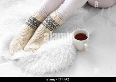 Pieds femelles dans des chaussettes avec tasse de thé on bed Banque D'Images