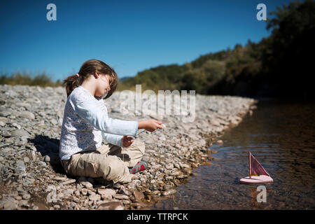 Bateau jouet fille tirant avec une corde en position assise au Lakeshore sur sunny day Banque D'Images
