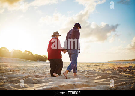 Senior couple holding hands en marchant sur une plage de sable de journée ensoleillée Banque D'Images