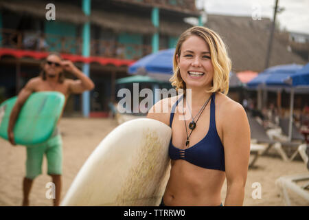 Portrait of happy woman in bikini with surfboard on beach at debout Banque D'Images