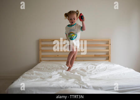 Toute la longueur de playful girl jumping on lit dans la chambre Banque D'Images