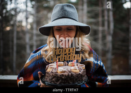 Cheerful woman holding birthday cake tout en se tenant à l'extérieur pendant l'hiver Banque D'Images