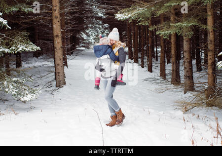 Fille heureuse mère portant en position debout en forêt durant l'hiver Banque D'Images