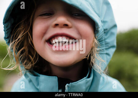 Close-up portrait of cute happy girl in blue raincoat debout contre des plantes pendant la saison des pluies Banque D'Images