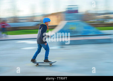 Vue latérale des jeunes patineurs de porter un casque bleu en mouvement au skatepark Banque D'Images
