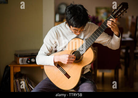 L'homme qui joue de la guitare tout en restant assis à la maison Banque D'Images