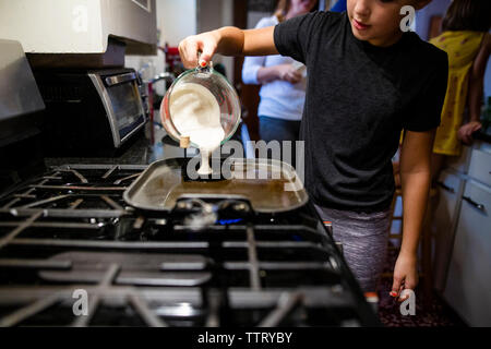 Portrait of Girl Faire des crêpes sur la cuisinière en position debout contre la famille dans la cuisine Banque D'Images