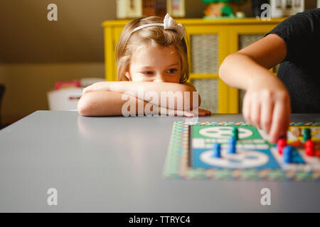 Cute girl looking at sœur jouant ludo sur table en chambre Banque D'Images