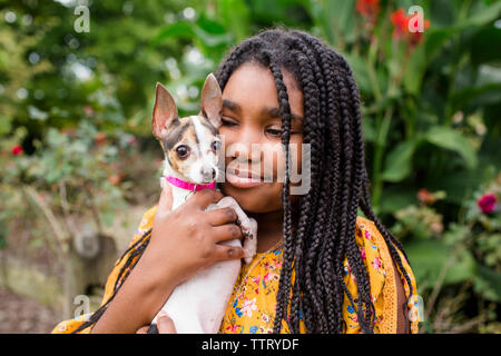 Close-up of smiling girl exerçant son mignon Chihuahua debout contre des plantes dans le parc Banque D'Images