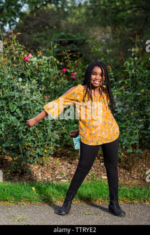 Portrait of happy girl dancing en se tenant sur le trottoir contre des plantes dans le parc Banque D'Images