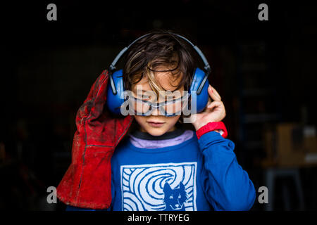 Close-up of boy portant des vêtements de travail à la recherche vers le bas tout en se tenant dans une forge Banque D'Images