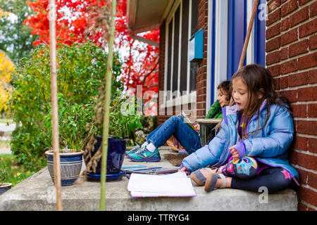 Deux enfants lire ensemble à l'extérieur sur leur front stoop Banque D'Images