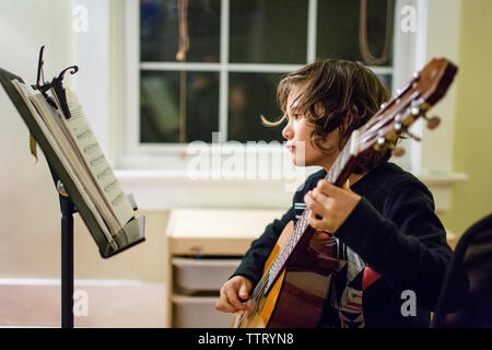 Un jeune garçon guitare pratique la nuit en face de la fenêtre Banque D'Images