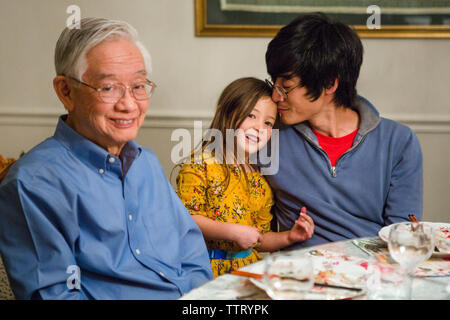 Une jolie petite jeune fille se tient avec son père et son grand-père à la table Banque D'Images