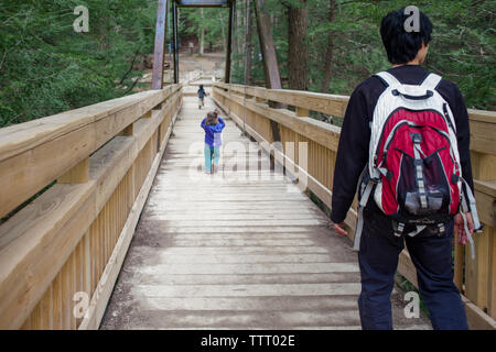 Un père traverse un long pont en bois en bois avec deux petits enfants Banque D'Images