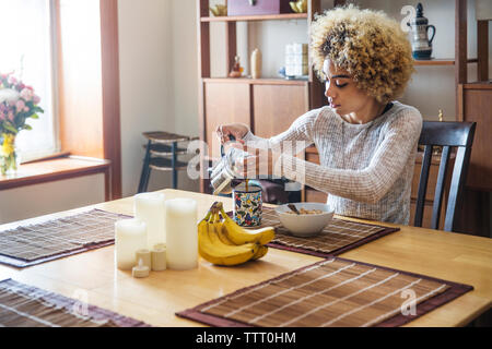 Dans Woman pouring Coffee cup at table in house Banque D'Images