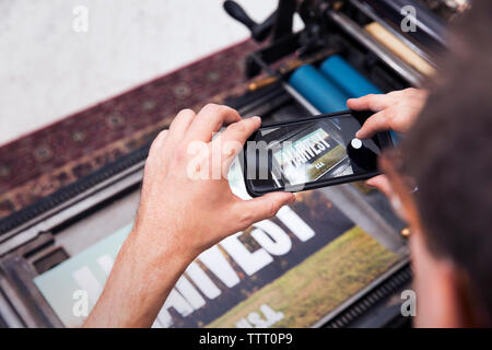 Portrait of man photographing poster imprimé avec smart phone Banque D'Images