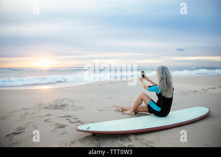 Vue de côté de surfer à travers la photographie smart phone while sitting on surfboard à Delray Beach Banque D'Images