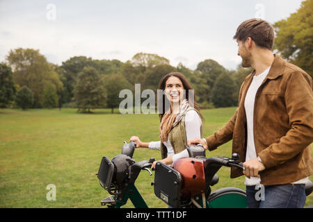 Couple heureux de parler tout en marchant avec des vélos en stationnement Banque D'Images