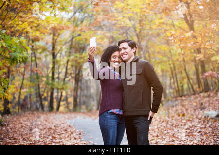 Couple heureux de prendre tout en selfies debout sur sentier en forêt Banque D'Images
