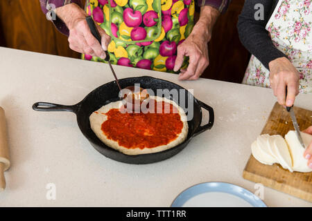 Portrait de l'homme application ingrédients sur la pâte à pizza dans une poêle pendant la découpe du fromage à la maison femme Banque D'Images