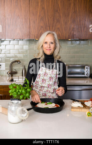 Portrait of smiling senior woman preparing pizza dans la cuisine à la maison Banque D'Images