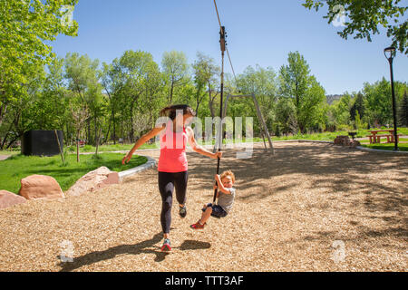 Toute la longueur du tirant mère zip line avec fils tout en jouant au jeu pour enfants en été Banque D'Images