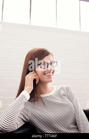 Smiling businesswoman sitting against wall at office Banque D'Images