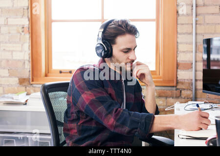 homme d'affaires portant des écouteurs écrivant sur le journal tout en travaillant dans le bureau Banque D'Images