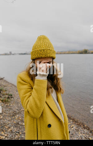 Woman with hand on face portant manteau d'hiver tout en se tenant au Lakeshore Banque D'Images