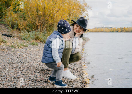 Mère avec mignon fils bénéficiant au lakeshore contre ciel nuageux dans le parc en automne Banque D'Images