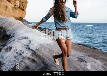 Portrait d'une femme s'exécutant sur des formations rocheuses avec mer en arrière-plan Banque D'Images