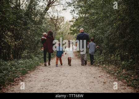 Vue arrière du family en marchant sur un chemin de terre au milieu des forêts Banque D'Images