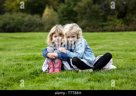 Deux sœurs sitting on grass smiling vers caméra reliée arms Banque D'Images