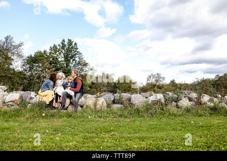 Famille de quatre assis sur un mur de pierre avec un ciel bleu au-dessus Banque D'Images