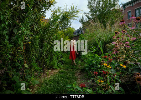 Fille qui marche à travers le jardin luxuriant en robe orange Banque D'Images