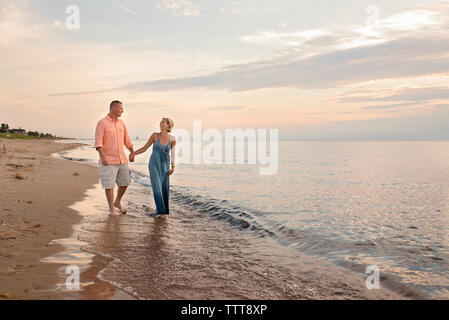 Couple d'amoureux se tenant la main tout en marchant sur le rivage à Beach pendant le coucher du soleil Banque D'Images