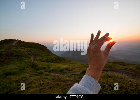 Illusion d'optique de main tenant bien sur la colline pendant le coucher du soleil Banque D'Images