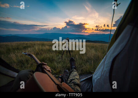 La section basse de l'homme qui joue de la guitare en position assise, dans une tente sur ciel contre la montagne pendant le coucher du soleil Banque D'Images