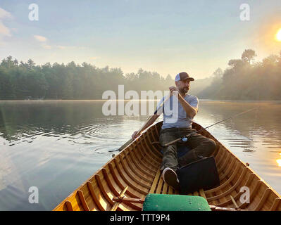 L'homme à la voiture tout en bateau à rames sur le lac contre le ciel au coucher du soleil Banque D'Images